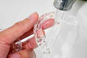 Patient rinsing clear aligner with water in sink