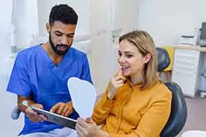 Smiling patient looking a reflection in handheld mirror with dentist