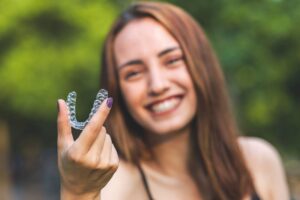 Woman outside smiling holding Invisalign with 2 fingers with purple nails